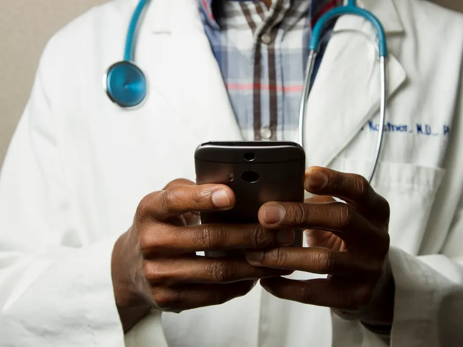 Healthcare provider in a white coat with a stethoscope, messaging a patient on a smartphone